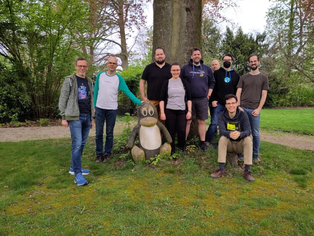 Foto von Mitgliedern der Netzbegrünung vor einem Baum um eine Statue des Linux Pinguin Maskottchens "Tux"