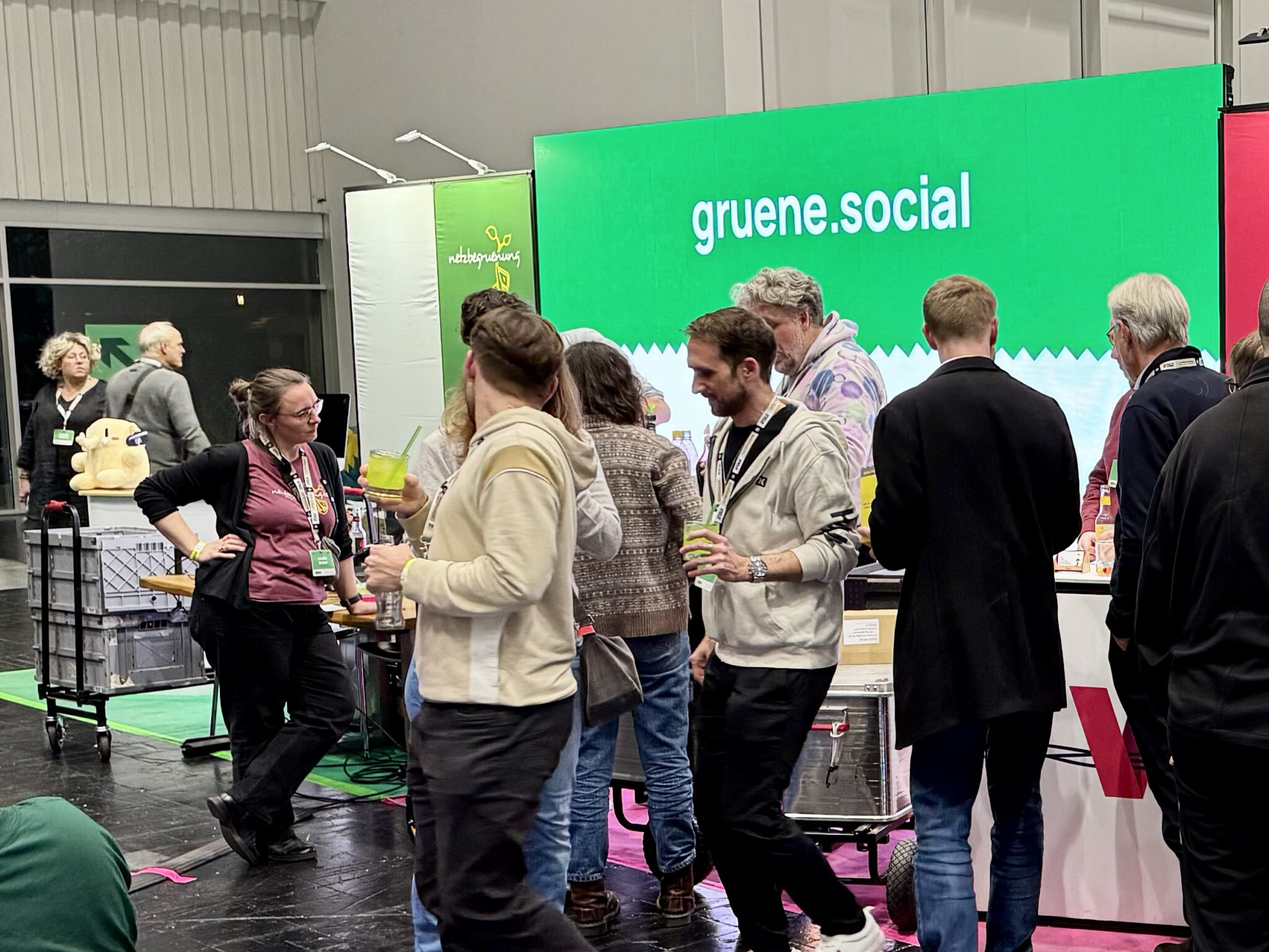 Mehrere Menschen stehen vor einem Messestand, dahinter sieht man eine LED-Wand auf der gruene.social geschrieben steht.