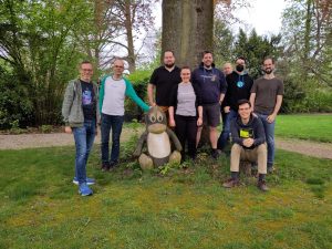 Foto von Mitgliedern der Netzbegrünung vor einem Baum um eine Statue des Linux Pinguin Maskottchens "Tux"